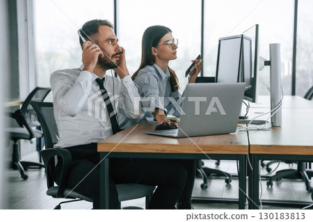 By the table with laptop. Two employees are working in the office together 130183813