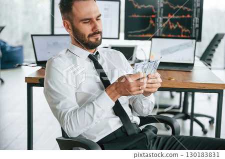 Counts money. Businessman is sitting by computer and working in the office Counts money. Businessman is sitting by computer and working in the office 130183831