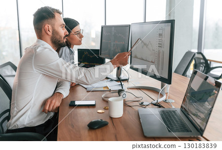 By the pc monitors. Two employees are working in the office together 130183839
