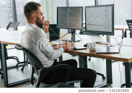 Side view. Businessman is sitting by computer and working in the office Side view. Businessman is sitting by computer and working in the office 130183940