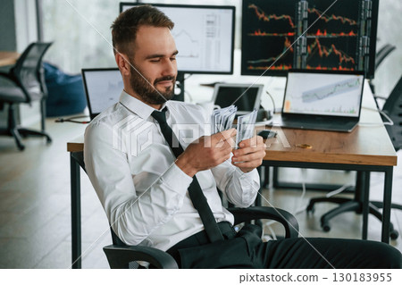 Counts money. Businessman is sitting by computer and working in the office Counts money. Businessman is sitting by computer and working in the office 130183955