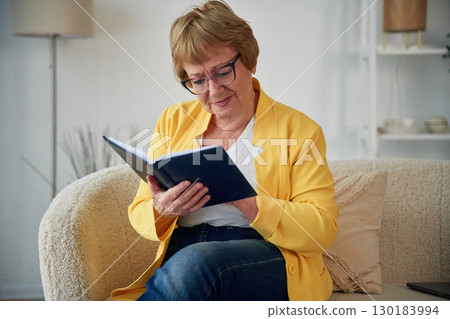 With book. Senior elderly woman is at home in the living room With book. Senior elderly woman is at home in the living room 130183994