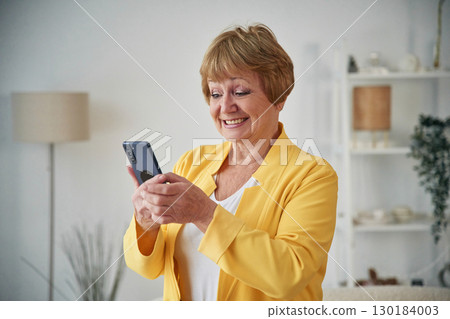 Holding smartphone. Senior elderly woman is at home in the living room 130184003