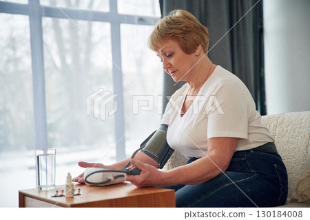 Measures blood pressure. Senior elderly woman is at home in the living room Measures blood pressure. Senior elderly woman is at home in the living room 130184008