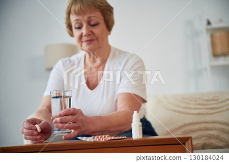 Taking the medicine, conception of illness. Senior elderly woman is at home in the living room 130184024