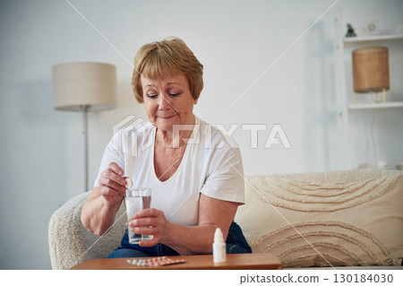 Self medicate. Taking medicine. Senior elderly woman is at home in the living room Self medicate. Taking medicine. Senior elderly woman is at home in the living room 130184030