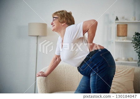 Back pain. Senior elderly woman is at home in the living room Back pain. Senior elderly woman is at home in the living room 130184047