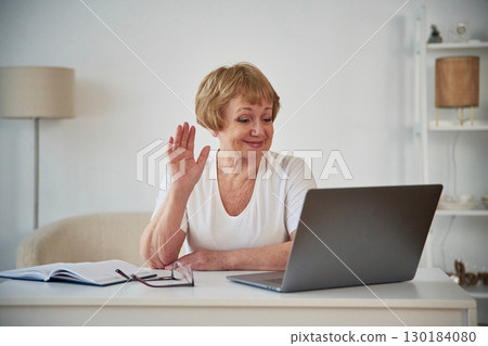 Silver colored laptop. Sitting by the table. Senior elderly woman is at home in the living room 130184080
