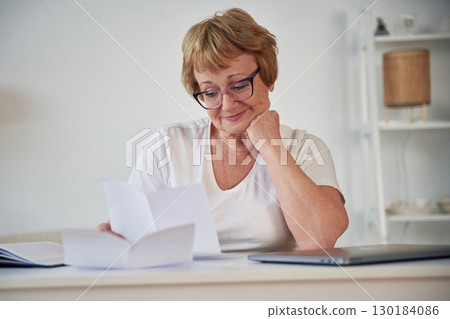 Reading the information from paper. Senior elderly woman is at home in the living room 130184086