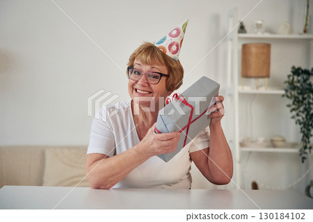 Celebrating birthday. With gift in the present box. Senior elderly woman is at home in the living room 130184102