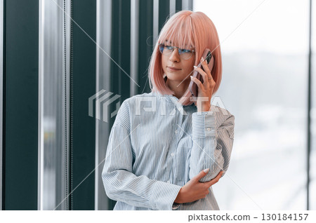 Talking by phone. Woman with pink hair is in the office. Young worker Talking by phone. Woman with pink hair is in the office. Young worker 130184157