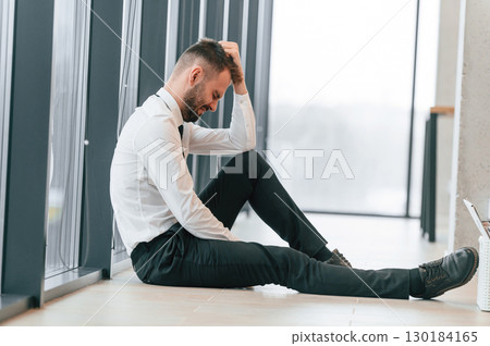 Depressive office worker is sitting on the floor, side view Depressive office worker is sitting on the floor, side view 130184165