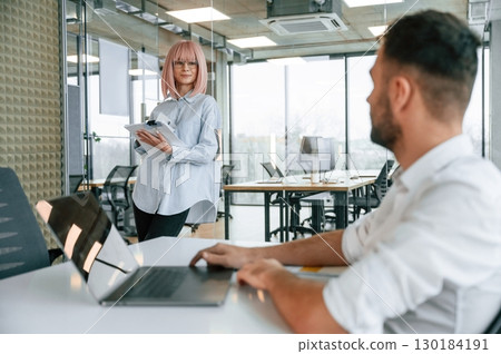 Boss is sitting by the table with laptop. Man and woman are working in the office together 130184191