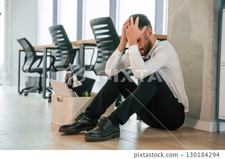 Depressed, sitting on the floor. Unemployed man is with personal belongings after being fired 130184294
