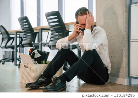 Depressed, sitting on the floor. Unemployed man is with personal belongings after being fired Depressed, sitting on the floor. Unemployed man is with personal belongings after being fired 130184296