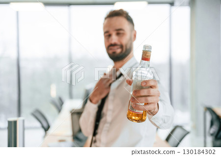 Holding bottle with whiskey. Businessman in office with alcohol 130184302