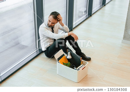 By the panoramic windows, sitting. Unemployed man is with personal belongings after being fired 130184308