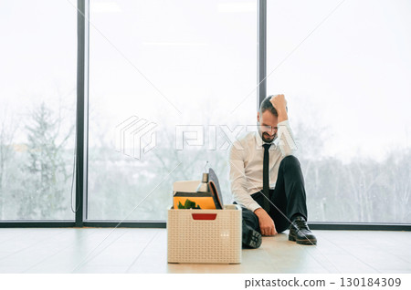 By the panoramic windows, sitting. Unemployed man is with personal belongings after being fired 130184309
