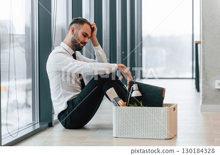 Feeling bad, sitting on floor. Unemployed man is with personal belongings after being fired 130184328