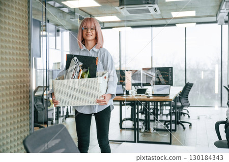 Standing and smiling. Unemployed woman with pink hair is with personal belongings after being fired Standing and smiling. Unemployed woman with pink hair is with personal belongings after being fired 130184343