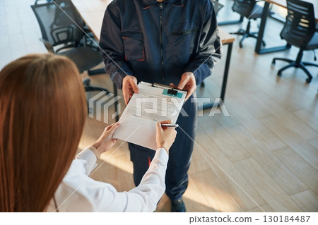 Sign this document. Man and woman employees are working in the office Sign this document. Man and woman employees are working in the office 130184487