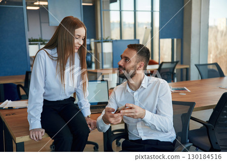 Showing information in the phone. Man and woman employees are working in the office Showing information in the phone. Man and woman employees are working in the office 130184516