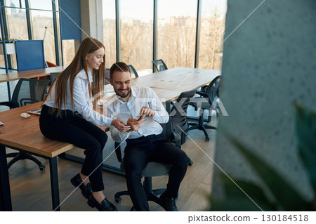 Showing information in the phone. Man and woman employees are working in the office Showing information in the phone. Man and woman employees are working in the office 130184518