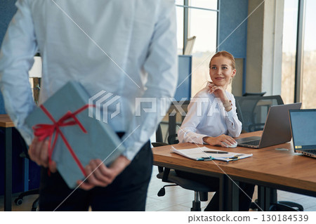 Holding gift box for woman. Two employees are working in the office 130184539