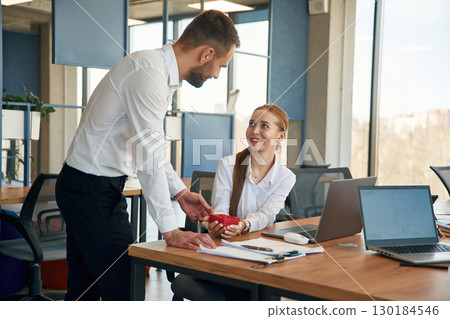 Surprise for woman. Little red gift box. Two employees are working in the office Surprise for woman. Little red gift box. Two employees are working in the office 130184546