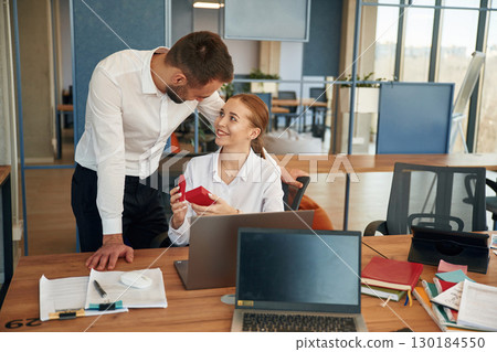 Surprise for woman. Little red gift box. Two employees are working in the office 130184550