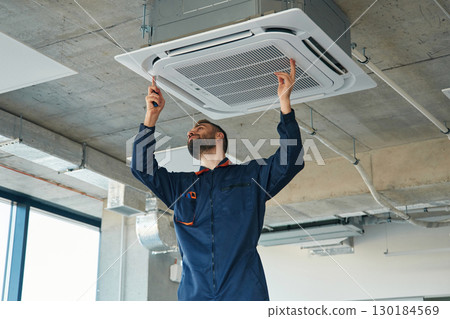 A man repairs the ventilation system, the device hangs on the ceiling A man repairs the ventilation system, the device hangs on the ceiling 130184569