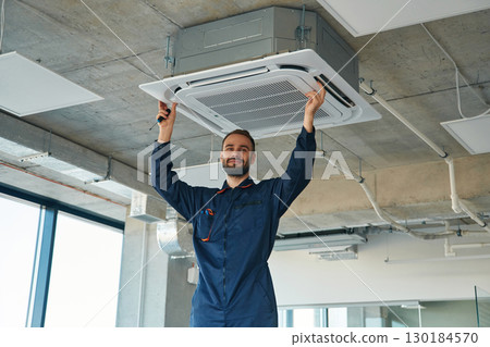 A man repairs the ventilation system, the device hangs on the ceiling 130184570