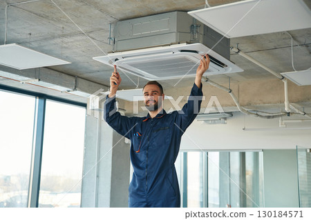A man repairs the ventilation system, the device hangs on the ceiling 130184571