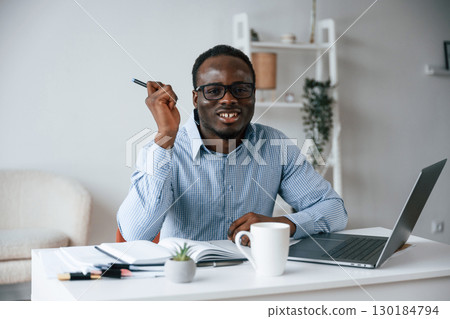 Sitting and smiling. With pen in hand. Businessman is working in the office by laptop 130184794
