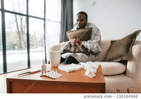 Sitting on sofa, holding pillow. Sick black man is at home 130184988