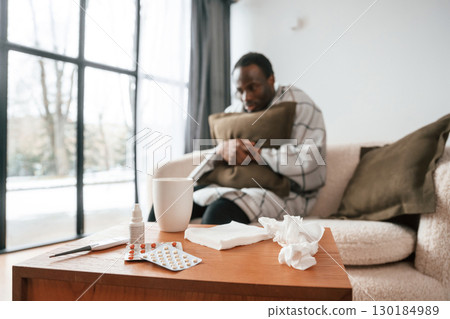 Sitting on sofa, holding pillow. Sick black man is at home 130184989