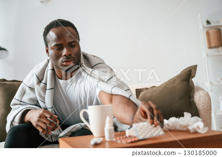 Holding pills that are on the table. Sick black man is at home Holding pills that are on the table. Sick black man is at home 130185000