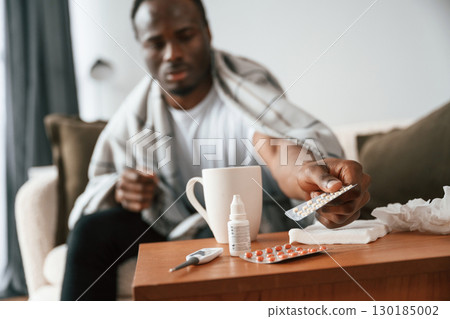 Holding pills that are on the table. Sick black man is at home Holding pills that are on the table. Sick black man is at home 130185002