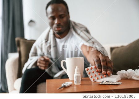 Holding pills that are on the table. Sick black man is at home Holding pills that are on the table. Sick black man is at home 130185003