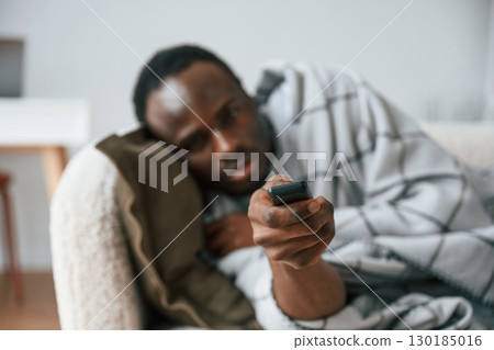Holding TV remote controller. Lying down. Sick black man is at home 130185016
