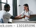 Sitting by a table. Female doctor measures blood pressure of a man 130185096