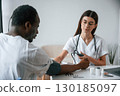 Sitting by a table. Female doctor measures blood pressure of a man 130185097