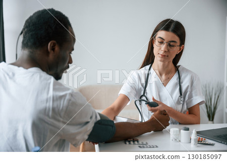 Sitting by a table. Female doctor measures blood pressure of a man 130185097