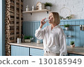Healthy Lifestyle A Woman Delightfully Enjoying a Refreshing Beverage in a Modern and Stylish Kitchen Space 130185949