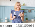 An Elegant Woman Joyfully Toasting with a Glass of Rich Red Wine in a Beautifully Stylish Kitchen Space 130185964