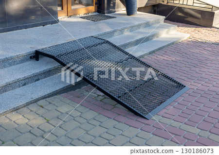 A metal ramp is positioned at the entryway of a building, providing accessibility for those with mobility challenges on a sunny day A metal ramp is positioned at the entryway of a building, providing accessibility for those with mobility challenges on a sunny day 130186073