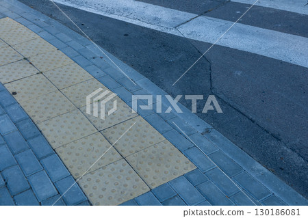 A close-up of a crosswalk area showing textured paving blocks and a clear path, highlighting urban design in a city setting A close-up of a crosswalk area showing textured paving blocks and a clear path, highlighting urban design in a city setting 130186081