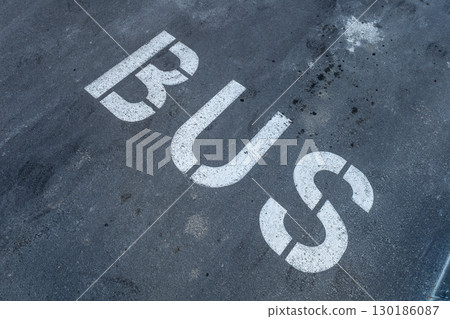 A large 'BUS' sign is painted on the ground in a parking area, indicating a designated spot for buses in an urban environment A large 'BUS' sign is painted on the ground in a parking area, indicating a designated spot for buses in an urban environment 130186087