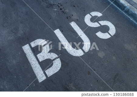 Bold white lettering clearly marks the bus stop area on the pavement in an urban setting under bright daylight Bold white lettering clearly marks the bus stop area on the pavement in an urban setting under bright daylight 130186088