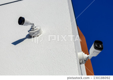Two security cameras are installed on the corner of a contemporary building, monitoring the surroundings under a clear blue sky Two security cameras are installed on the corner of a contemporary building, monitoring the surroundings under a clear blue sky 130186092